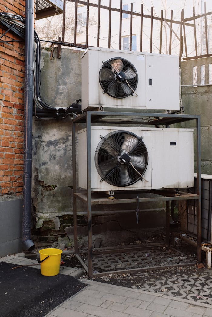 gallery-4 Two industrial air conditioning units mounted outdoors against a brick wall, emphasizing HVAC technology.